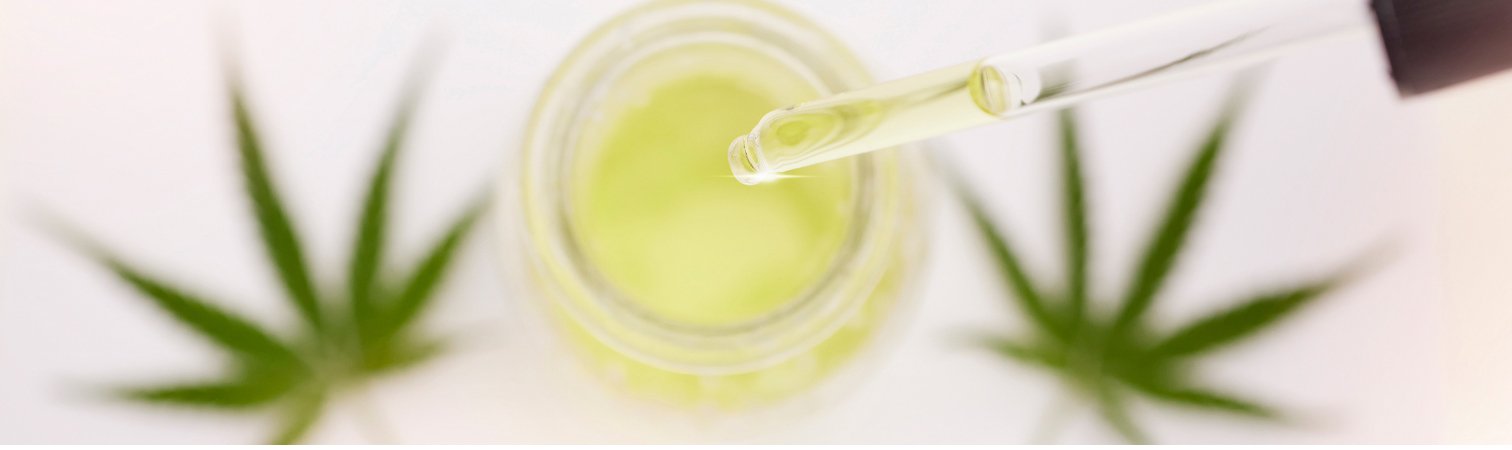 A jar of cbd oil flanked by cannabis leaves.